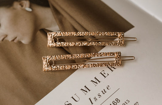 Set of two gold textured rectangle metal hairpins displayed on a fashion magazine – elegant minimalist hair accessories for everyday styling or special occasions.