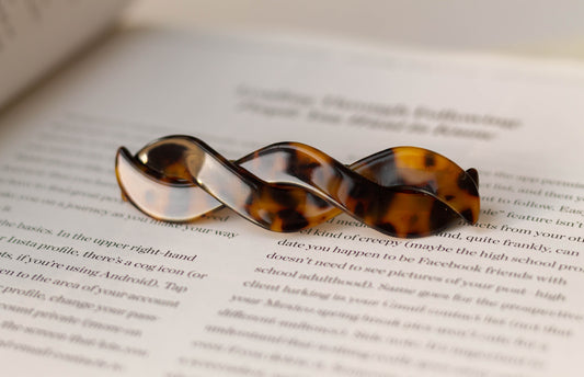 An acetate braid hair barrette clips in the colour classic tortoise placed on an open book.