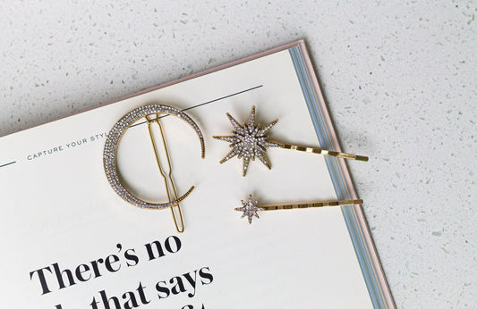 A set of three gold-colored hairpins in the shapes moon and stars with rhinestone crystal details, displayed on an open book.