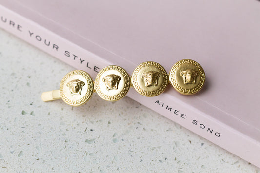 A gold medallion hairpin is placed on a pale pink surface with a book titled 'Capture Your Style' by Aimee Song in the background.
