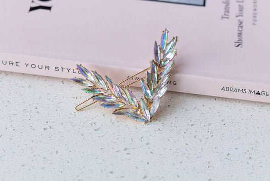 A V-shaped hairpin with multi-colored crystals adorning the barrette, placed on a surface next to a pink book with text.