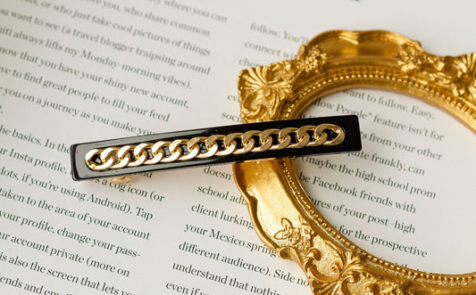 A gold chain hair barrette placed on an open book and golden frame, showcasing its elegant design.