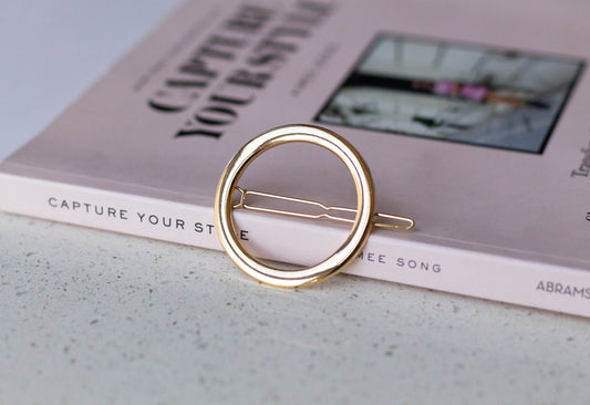 A gold-colored thick metal circle hairpin is placed on a book.