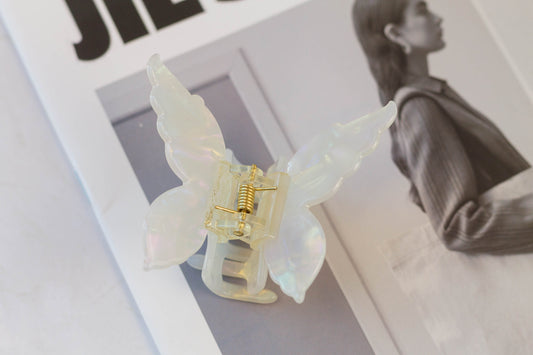 A white butterfly-shaped hair claw placed on an open book, with a person in the background.