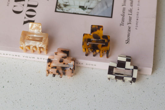 Four mini acetate hair claws in different colors placed on a surface, with all of them resting on a fashion book.