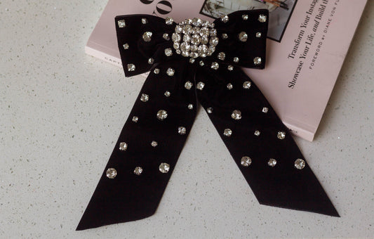 Black velvet hair bow barrette embellished with sparkling crystal rhinestones, styled on a pink fashion book – elegant statement accessory for special occasions or glam looks.
