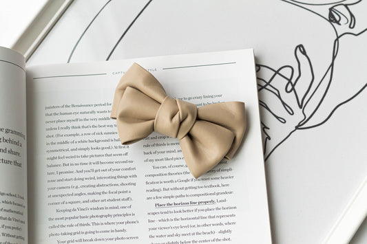 A beige faux leather hair bow clip placed on an open book.