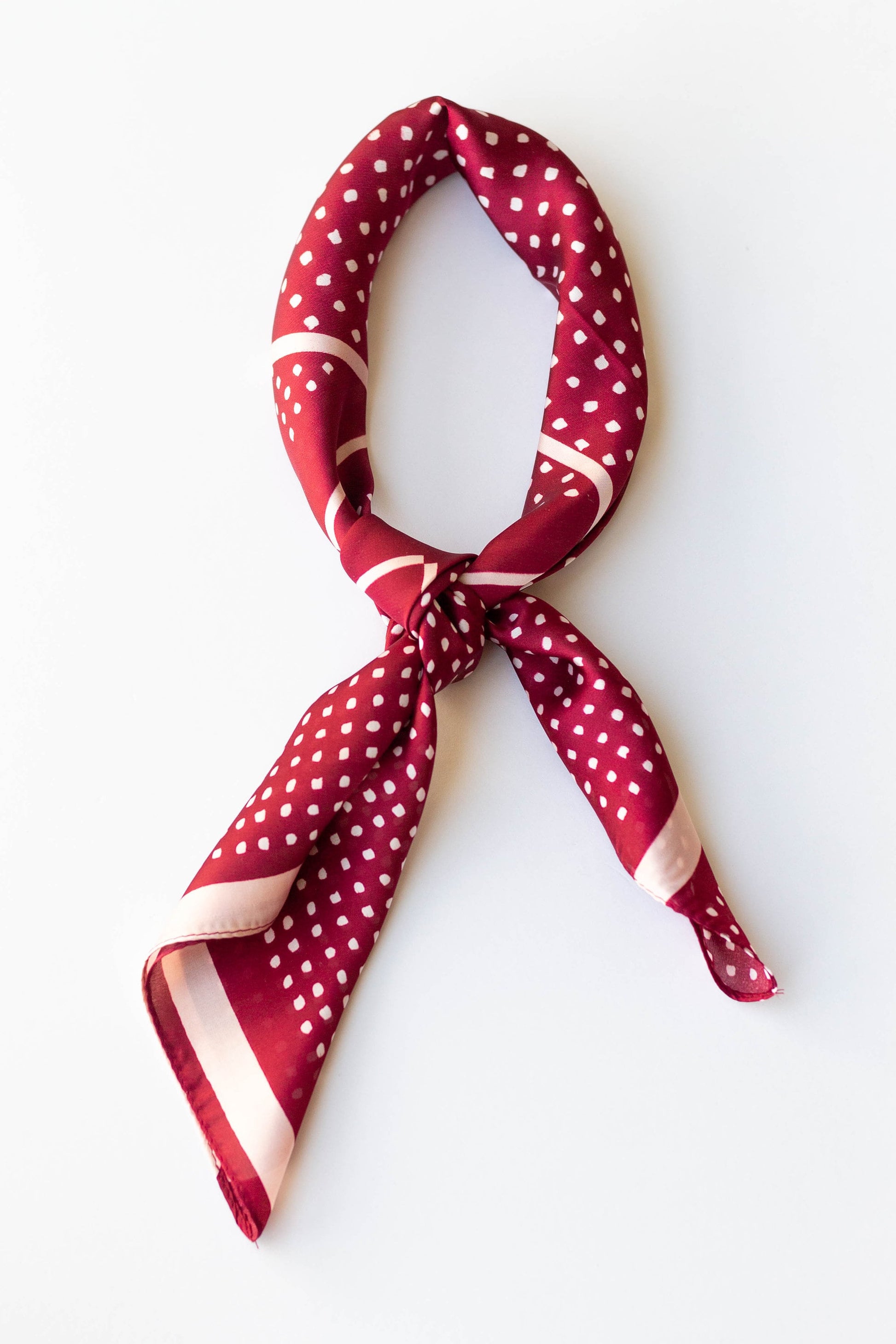 A silky red hair scarf with a white polka-dot pattern, tied in a knot.