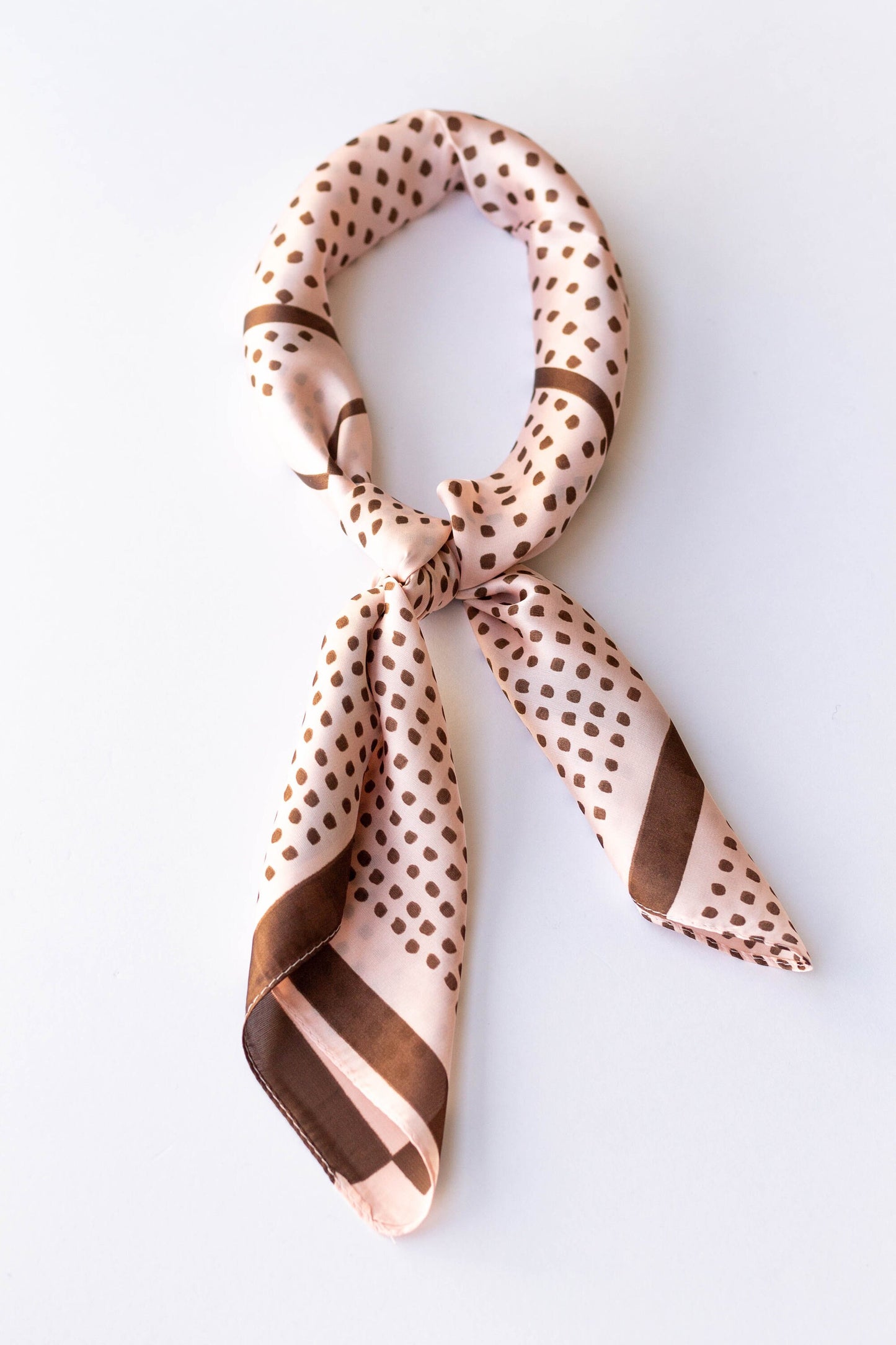 A silky beige hair scarf with a brown polka-dot pattern, tied in a knot.