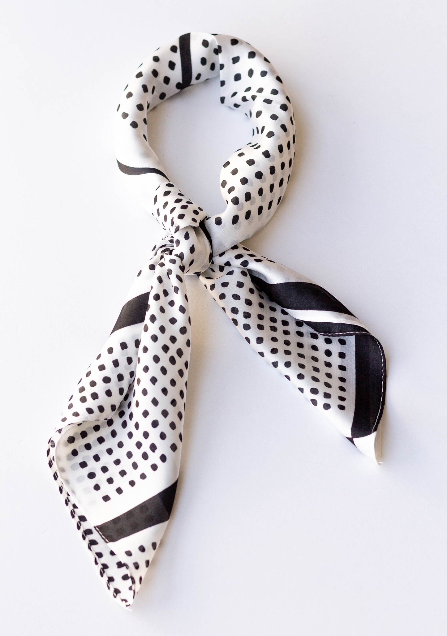 A silky white hair scarf with a black polka-dot pattern, tied in a knot.
