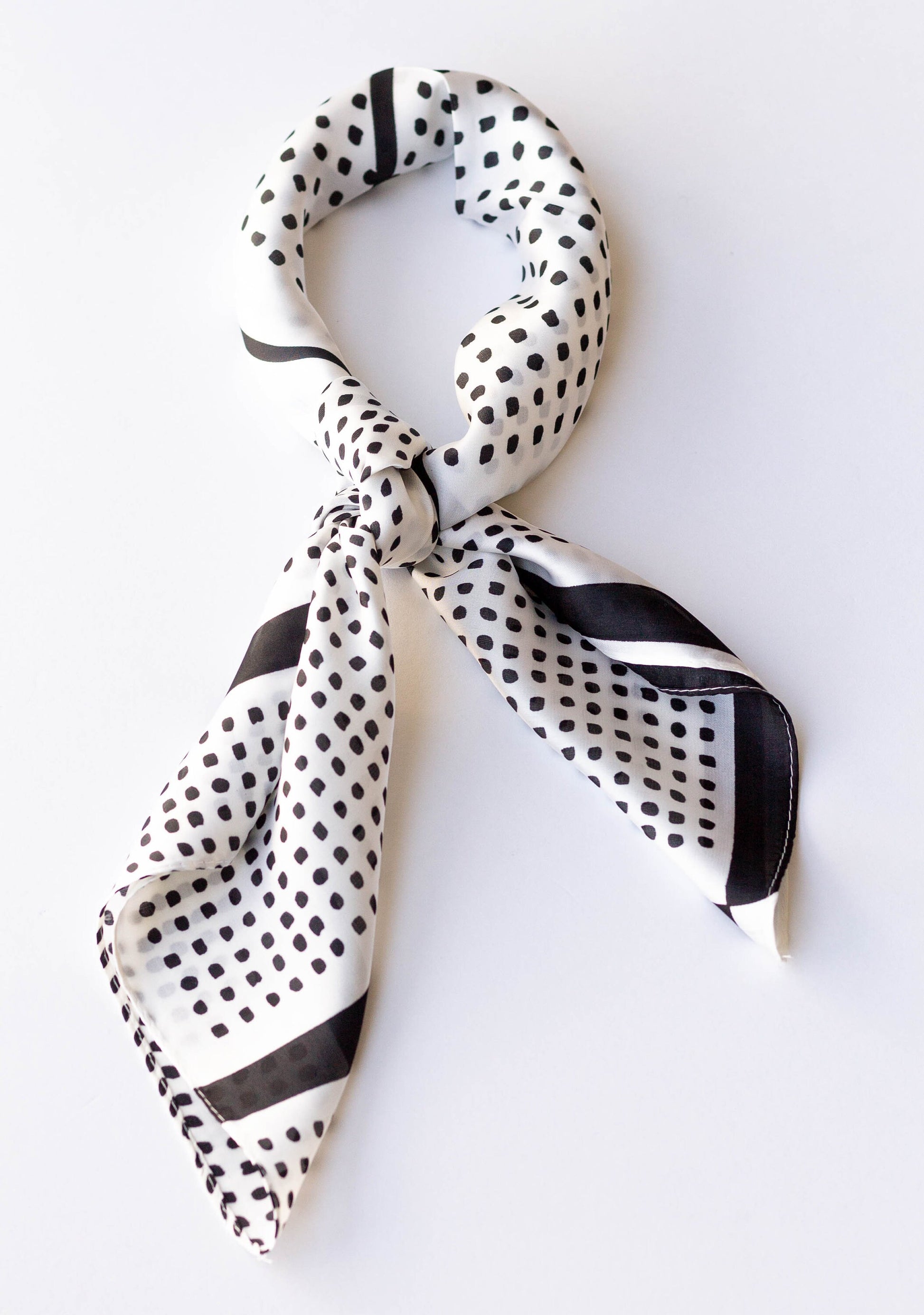 A silky white hair scarf with a black polka-dot pattern, tied in a knot.